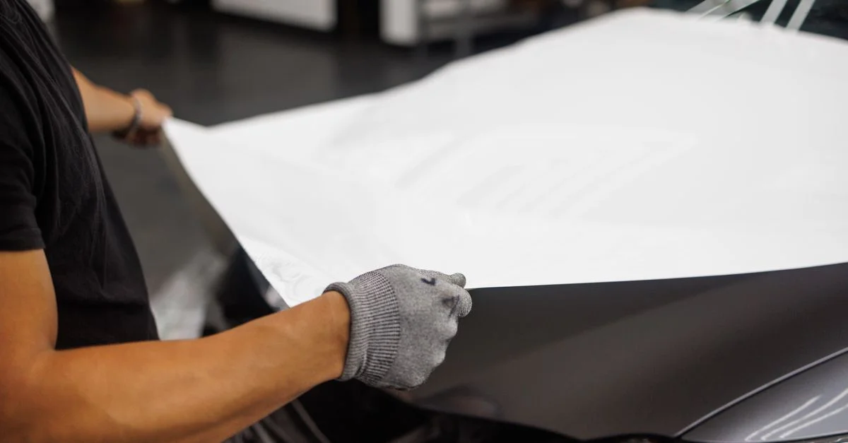 Personne appliquant un film vinyle sur le capot de voiture dans un garage.