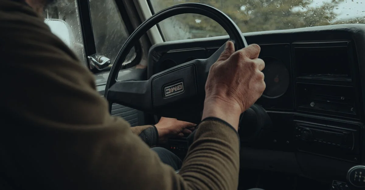 Gros plan sur une personne au volant d'un véhicule avec une forêt luxuriante visible à travers le pare-brise.