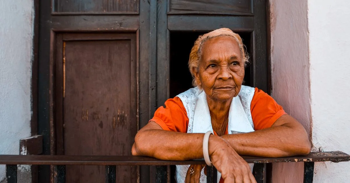 Femme senior en chemise orange s'appuyant sur un balcon en fer.